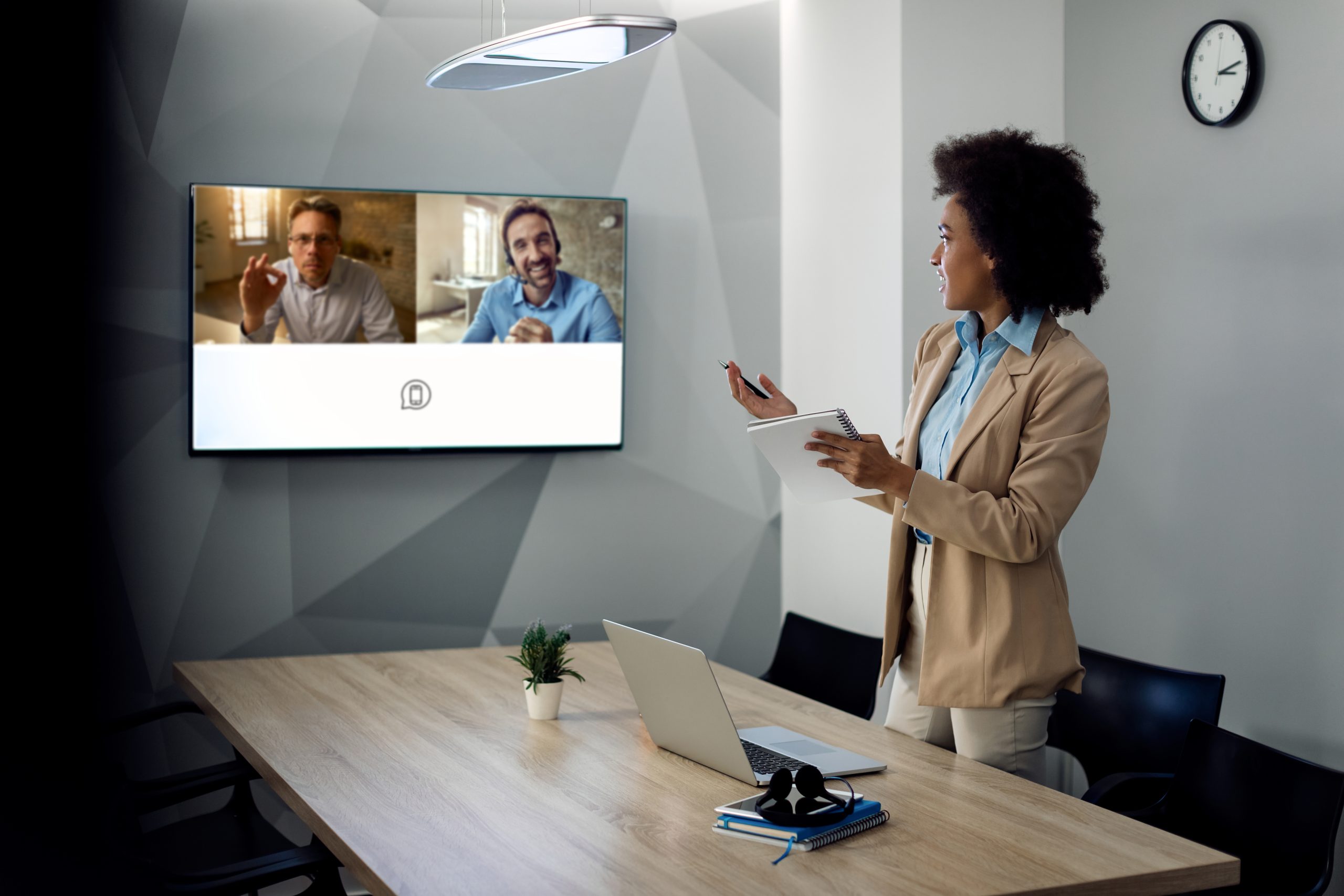 Black businesswoman looking at projection screen and communicating with coworkers during video call from the office. Copy space.